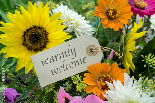 Colorful bouquet of summer flowers with card and english text: warmly welcome