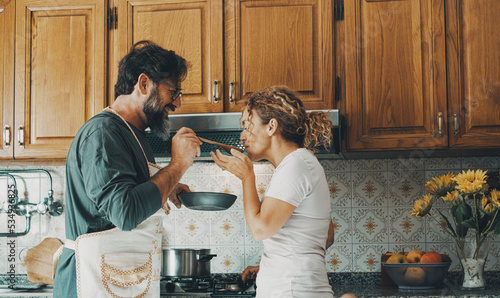 One happy real couple at home enjoying life together and relationship. Man giving food to woman to taste. Male people cooking for his wife. Male and female enjoying leisure activity indoor in kitchen