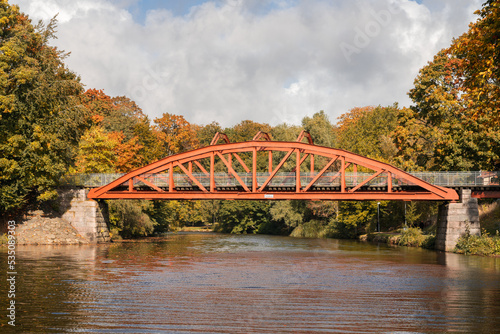 Autumn colors surrounds the red bridge Pyttebron over Ronne river which is built 1904 and still in use today in Angelholm, Sweden.