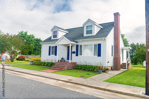 Cute brightly painted white shingled cottage with blue shutters. coastal town on cloudy day.