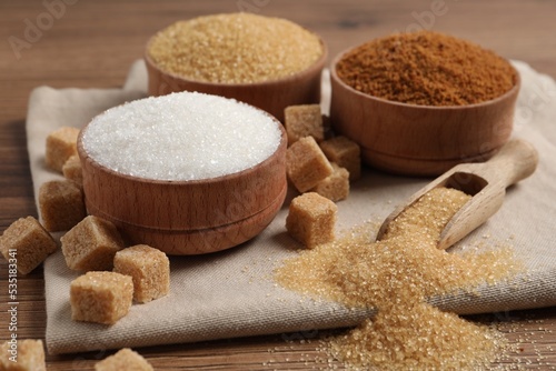 Different types of sugar in granules and cubes on wooden table, closeup