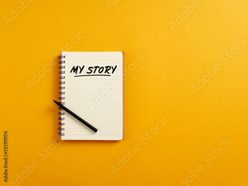 Notepad and black pen on yellow background with the handwritten word my story. Telling about yourself and biography