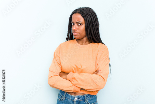 Young African American woman with braids hair isolated on blue background frowning face in displeasure, keeps arms folded.