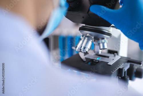 Scientist analyzing microscope slide at laboratory. Young woman technician is examining a histological sample, a biopsy in the laboratory of cancer research