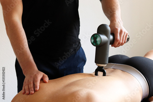 Sports percussion massage in medical room of gym. Masseur does massage exercises. Percussions therapy for regenerating massage of sport body. Concept of rehabilitation of sports injuries