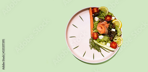 intermittent fasting concept plate as a clock with salad, salmon, fish and vegetables, tomato, lemon