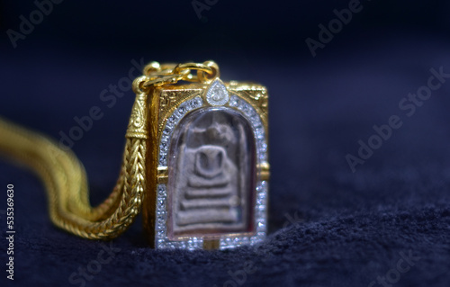 The golden Buddha amulet frame is shiny and placed on the ground.
