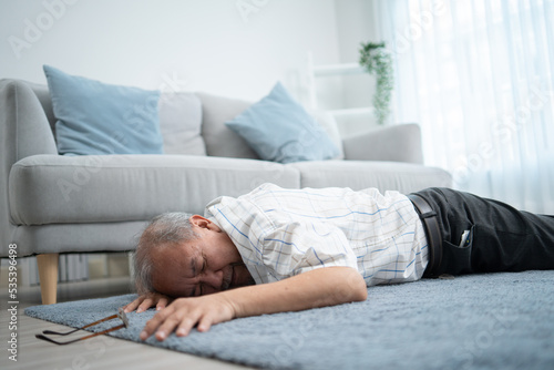 Asian senior grandfather fainting and falling on the ground in the living room. Elderly male patient having an accident or heart attack. home nursing and health insurance concept