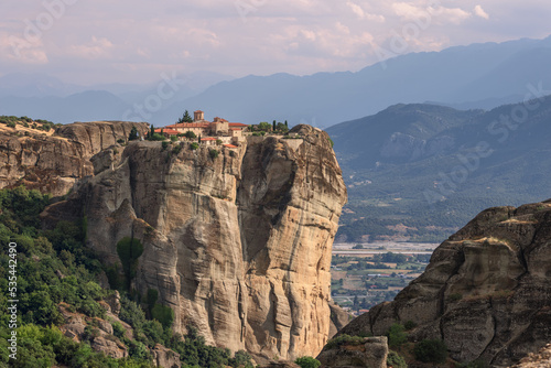 Panoramic photo of northwestern side of St Stephen Monastery with church built in 1798 and spacious plain with trees and mountains with gentle tones, Meteora, Greece