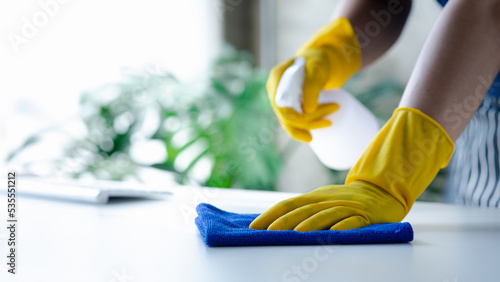 Person cleaning the room, cleaning staff is using cloth and spraying disinfectant to wipe the tables in the company office room. Cleaning staff. Maintaining cleanliness in the organization.