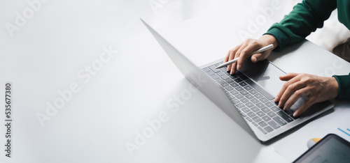 Close-up Businesswoman working online on the white table at office, hands holding pen and typing on laptop keyboard, online job concept.