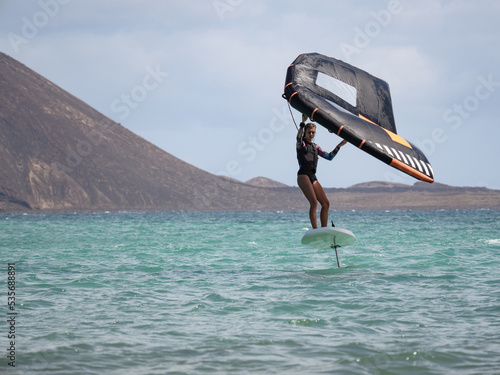 Caucasian young woman practicing water sport in the ocean wingfoil on hydrofoil surfboard