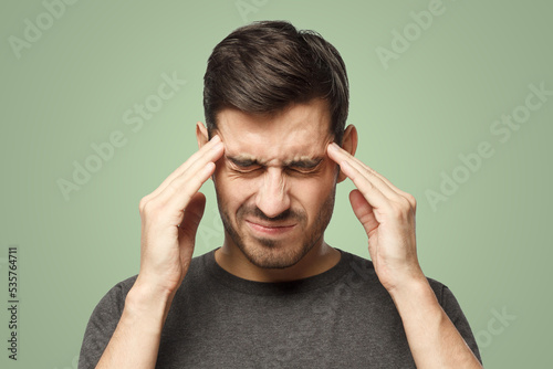 Man suffering from headache, pressing fingers to temples with closed eyes on green background
