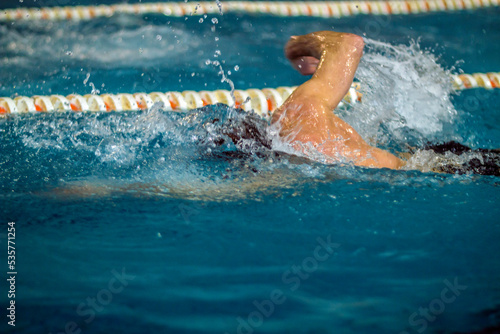 A swimmer in a competition swims quickly in a pool in clear blue water 