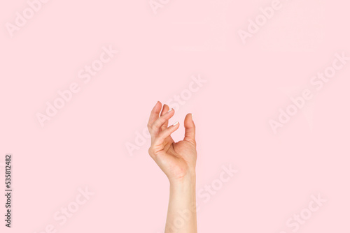 Mano de mujer en posición para sostener algo sobre un fondo rosa liso y aislado. Vista de frente y de cerca Copy space