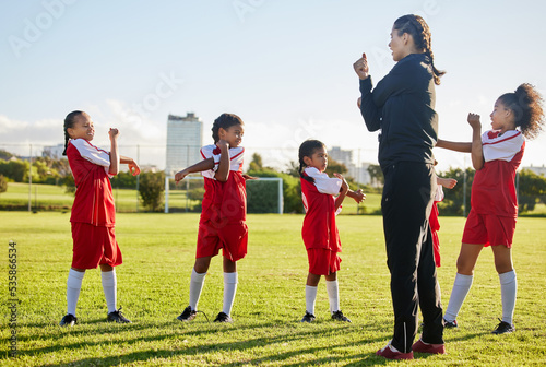 Fitness soccer, girl team and stretching with sport coach on sports field training, exercise or workout. Children, kids or coaching in diversity, teamwork and collaboration on warm up for game.