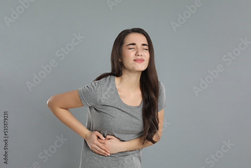 Young woman suffering from liver pain on grey background
