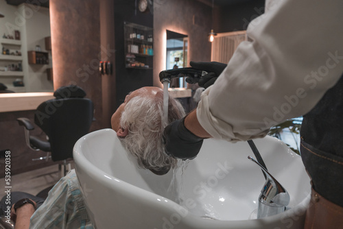 Detalle de peluquero lavando el pelo a un cliente senior, en la peluquería.