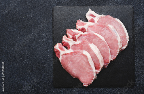 Raw pork chops, meat on slate board prepared for cooking. Black kitchen table, top view