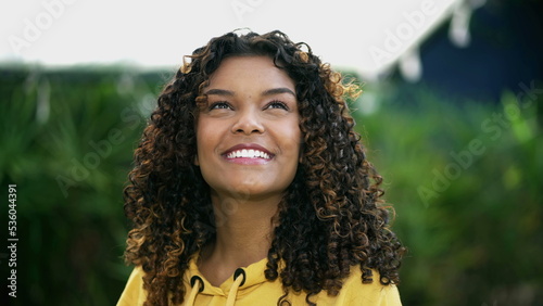 Hopeful young woman looking at sky with FAITH. One happy African American person closeup face standing outdoors