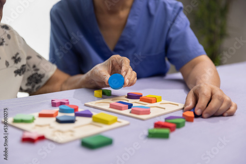 Caregiver and senior woman playing wooden shape puzzles game for dementia prevention