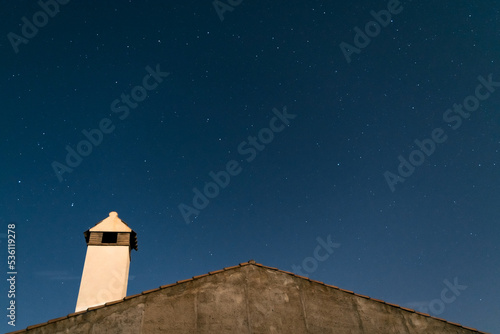 Cielo nocturno estrellado sobre el tejado con chimenea de una casa