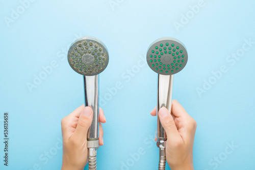 Woman hands holding new and old shower heads on light blue table background. Pastel color. Compare two objects with and without limescale. Dirty and clean. Closeup. Point of view shot. Top down view.