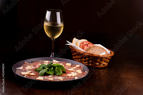 romantic dinner with carpaccio cold meat cattail basket of artisan breads basil leaves mustard dijon glass of white wine from the front