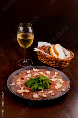 romantic dinner with carpaccio cold meats basket of artisan breads basil leaves mustard dijon glass of white wine wooden table in an angle portrait