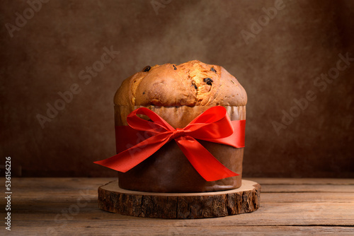 Traditional Italian Christmas Cake Panettone with red bow on wooden rustic background. Homemade artisan sourdough panettone ready for eating. Classic italian Christmas Food and Edible gift