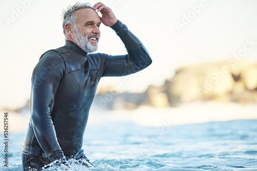 Beach, elderly surfer man in water and happy ocean holiday in Australia. Freedom, sea and happiness, fun on retirement surf vacation. Health, free time and sports in nature, a senior smile in waves.