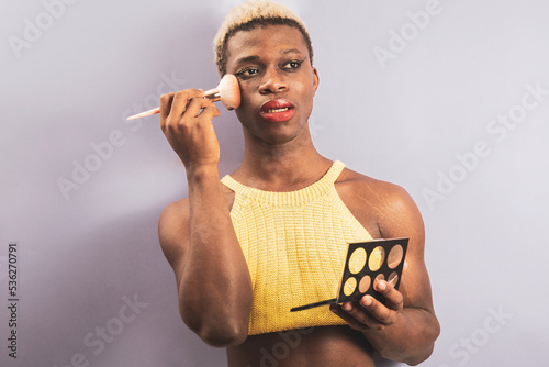 An androgynous black man posing on a purple studio background while putting on makeup.