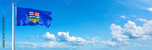 Alberta - state of Canada, flag waving on a blue sky in beautiful clouds - Horizontal banner 