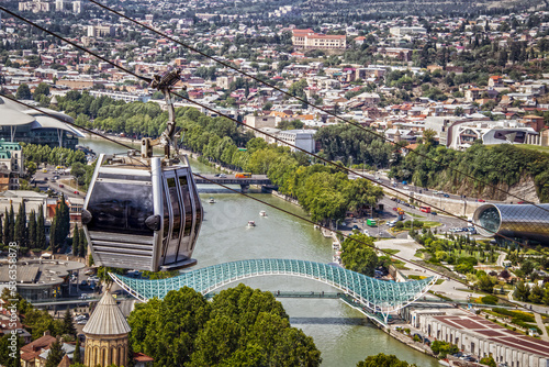 Close-up of Aerial Cable Car connecting Rike Park on the left bank of the Mtkvari river with Narikala Fortress in Tbilisi Georgia - river and Peace Bridge and busy city below