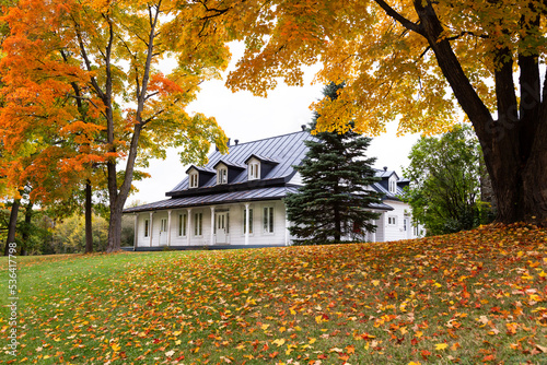 Low angle view of patrimonial French style 1861 white presbytery with black metal roof and dormer windows set in colourful foliage, Quebec City, Quebec, Canada