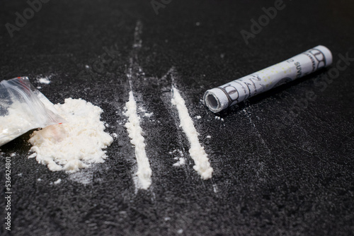 Plastic bag, two lines and a bunch of cocaine with a breathing tube with hundred dollar bill, on a black background, closeup.