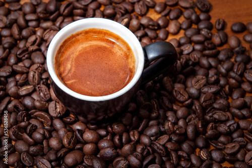 Kawa espresso w czarnej filiżance na stole pełnym świeżo palonych ziaren kawy
