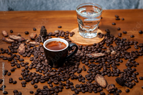 Kawa espresso w czarnej filiżance i szklanka wody na stole pełnym świeżo palonych ziaren kawy