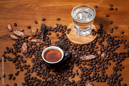 Czarna kawa espresso w czarnej filiżance i szklanka wody na stole pełnym świeżo palonych ziaren kawy