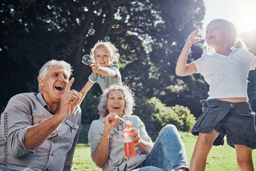 Grandparents, bubbles and children play in park happy together for fun, joy and outdoor happiness. Retired, smile and excited elderly senior couple, girl grandkids and love playing outside in nature