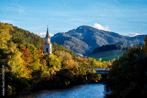 Church steeple among autumn trees against the backdrop of the Alpine mountains