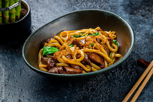 fried Udon with beef and vegetables on dark stone table