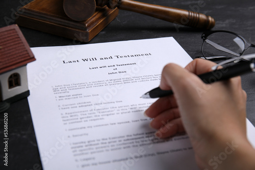 Woman signing last will and testament at black table, closeup