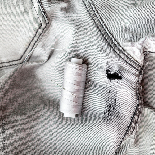 needle and thread on fabric. holes in gray jeans