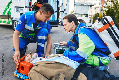 Paramedics immobilized senior patient with neck brace and spinal board to prevent damage in case of spinal injury. First aid from ambulance technicians