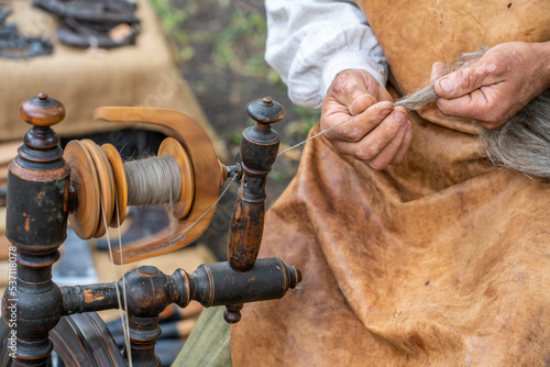 Russian man sitting and spinning a thread of sheep wool on an old spinning wheel