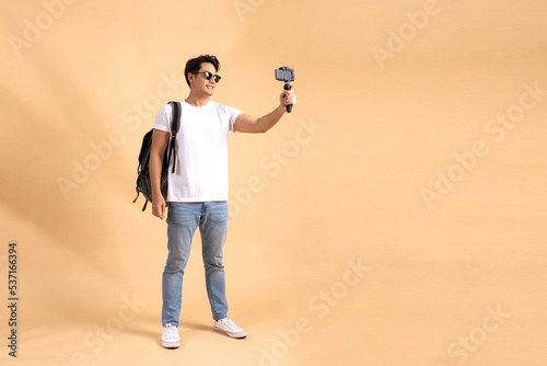 Young Asian tourist backpacker man smiling and taking a selfie and blog isolated on beige background