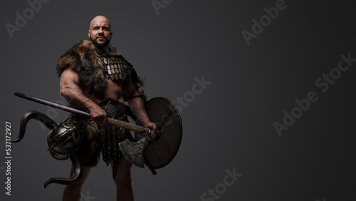 Studio shot of handsome ancient viking dressed in armor and fur holding axe and shield.