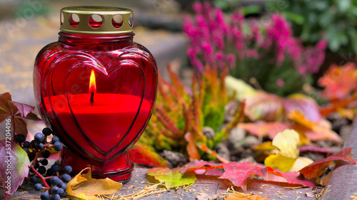 A red heart-shaped candle on a grave in a cemetery on an autumn day. All Saints Day. Copy space, shallow depth of field.