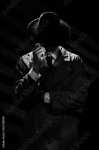 A dark silhouette of a man in a coat and hat in the noir style. A dramatic portrait in the style of detective films of the 1950s and 60s. The silhouette of a spy.